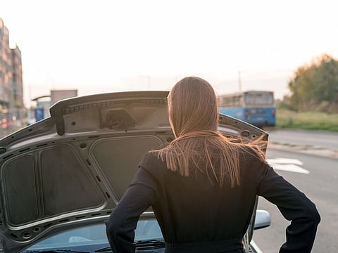 A woman looks under the hood of her broken car.