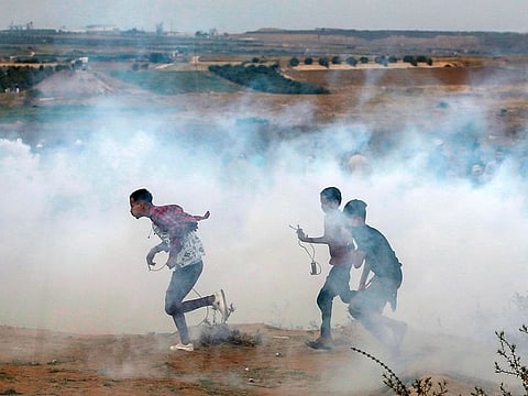 Palestinian protesters walk away through fumes from tear gas fired by Israeli forces across the barbed wire fence during a protest marking Al Quds (Jerusalem) International Day along the border near Bureij in the central Gaza Strip on May 31, 2019.