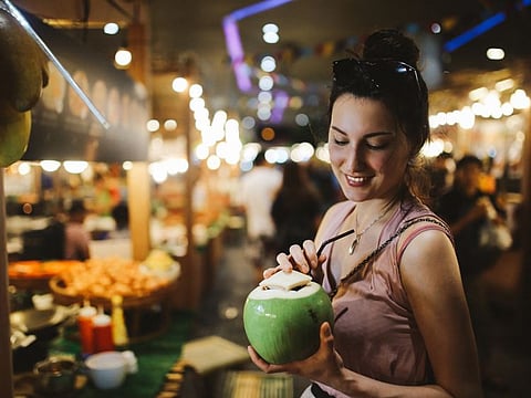 Authentic Thai street food in Bangkok. Young woman is having a refreshment with delicious coconut water on a hot summertime evening.
