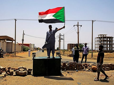 A Sudanese protester holds a national flag as he stands on a barricade along a street, demanding that the country's Transitional Military Council hand over power to civilians, in Khartoum, Sudan June 5, 2019.