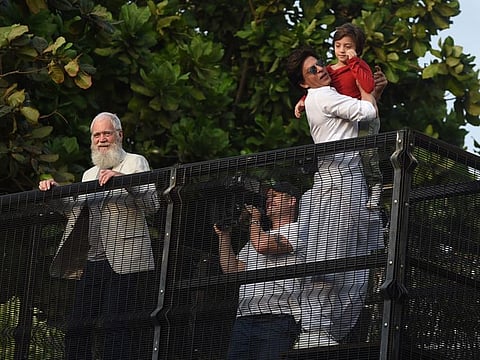 Bollywood actor Shah Rukh Khan (R) holds his son as he prepares to greet his fans during Eid al-fitr celebrations, next to US television host David Letterman (L) in Mumbai on June 5, 2019.