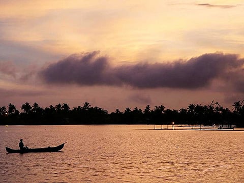 A man rows his boat in the tributary waters of Vembanad Lake against the backdrop of pre-monsoon clouds on the outskirts of Kochi, India