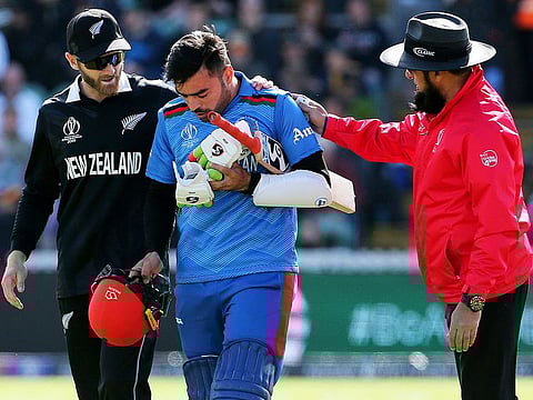 New Zealand's Kane Williamson, left and Umpire Aleem Dar help Rashid Khan, after a ball bowled by Lockie Ferguson bounced off Rashid's helmet and onto the stump during the World Cup group stage match between them, at the County Ground Taunton, England, on Saturday, June 8, 2019.