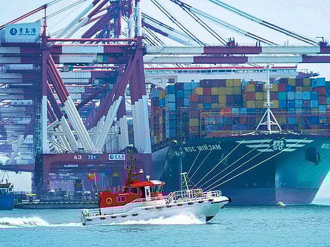 A boat sails past a cargo ship loading containers at a port in Qingdao in eastern China’s Shandong province, yesterday. China has reported a sharp jump in its trade surplus for May.