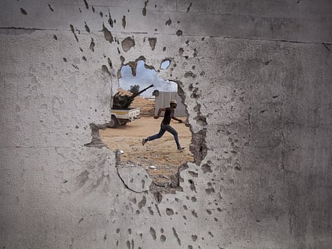 In this Oct. 7, 2011, file photo, a Libyan revolutionary fighter runs for cover while attacking pro-Gadhafi forces in Sirte, Libya, Friday, Oct. 7, 2011.