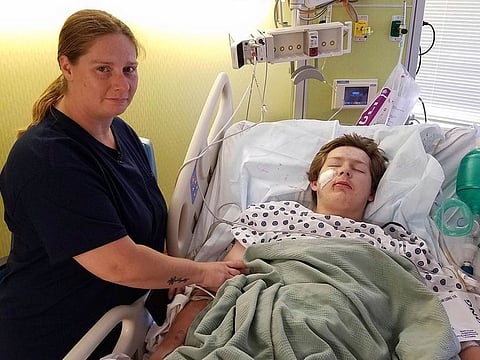 15-year-old Eli Gregg, right, recovers in the hospital bed in Kansas City, Kan., as his mother Jimmy Russell watches after doctors removed a 10" knife that impaled his face when he fell while playing.