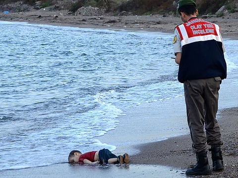 A Turkish police officer stands next to Alan Kurdi's body off the shores in Bodrum, southern Turkey, on September 2, 2015. This photo quickly became a defining image of the refugee crisis. (Nilufer Demir/AFP/Getty)