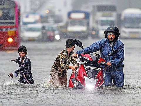 Commuters wade through a waterlogged street during heavy rain at Ghatkopar, in Mumbai.