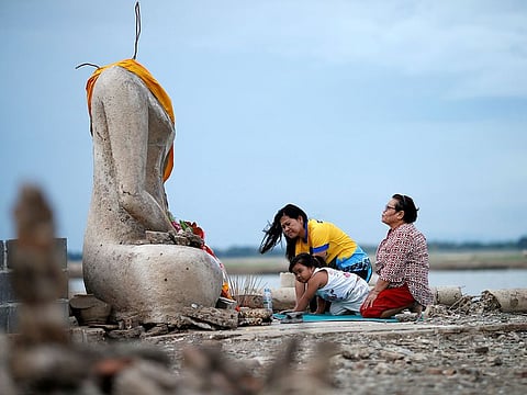 A family prays near the ruins of a headless Buddha statue, which has resurfaced in a dried-up dam due to drought, in Lopburi, Thailand.