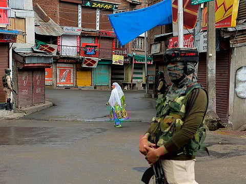 File image: In this picture taken on August 9, 2019 a woman walks past security personnel guarding a street in Srinagar as widespread restrictions on movement and a telecommunications blackout remained