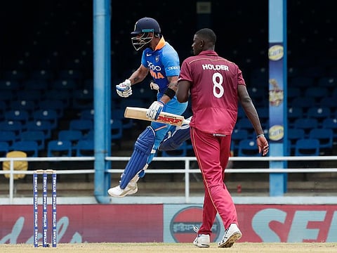 India's captain Virat Kohli jumps into the air while celebrating his century as West Indies captain Jason Holder looks on.
