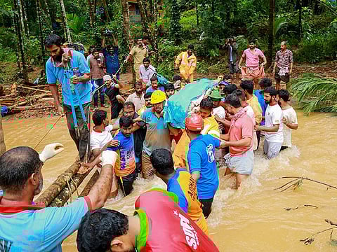 Rescue workers help locals who carry a dead body to cross a waterlogged area, after a landslide, at Kavalappara in Malappuram, on August 11, 2019.