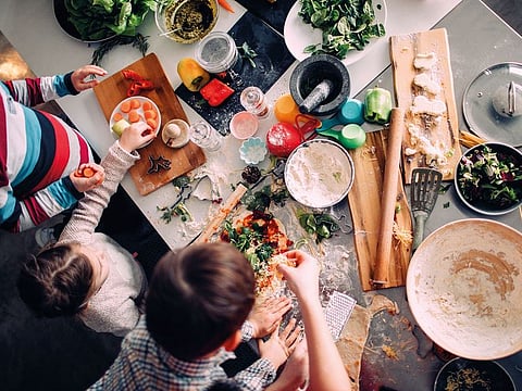 Children preparing pizza in the kitchen, with a little help from their mom