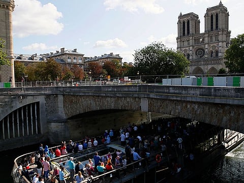 Tourists in a boat pass under a bridge near the Notre Dame cathedral in Paris.