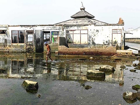 A man walks next to an abandoned submerged Mosque in northern Jakarta.