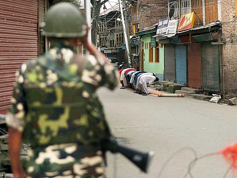 A paramilitary soldier stands guard as Kashmiri Muslims offer Friday prayers on a street outside a local mosque, amid restrictions, in Srinagar, India