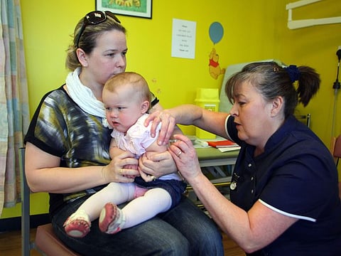 In this file photo taken on April 20, 2013 14-month-old Amelia Down sits on the lap of her mother Helen (L) as she receives the combined Measles Mumps and Rubella (MMR) vaccination at an MMR drop-in clinic at Neath Port Talbot Hospital near Swansea in south Wales on April 20, 2013.