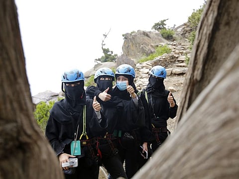Saudi tourists wear helmets and keep their faces and hair covered according to local custom, as they pose for a photo before zip lining between cliffs, during the al-Soudah festival in Abha, southwest Saudi Arabia.