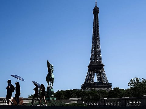 Tourist using umbrellas to protect themselves from a scorching sun walk on a bridge over the Seine river in front of the Eiffel Tower in Paris.