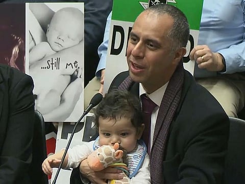 Mayor Jorge Elorza holds his son Omar as he testifies before the House Judiciary Committee at the Statehouse in Providence, Rhode Island.