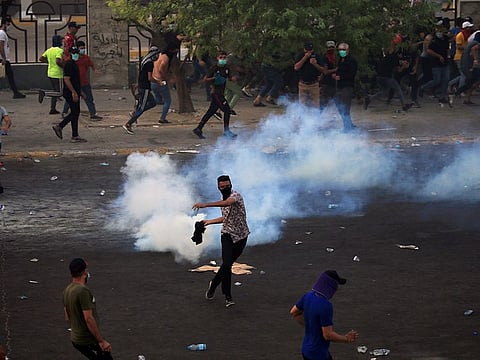 A demonstrator prepares to throw a tear gas canister used by Iraqi security forces as others disperse during a protest over unemployment, corruption and poor public services, in Baghdad, Iraq October 2, 2019.