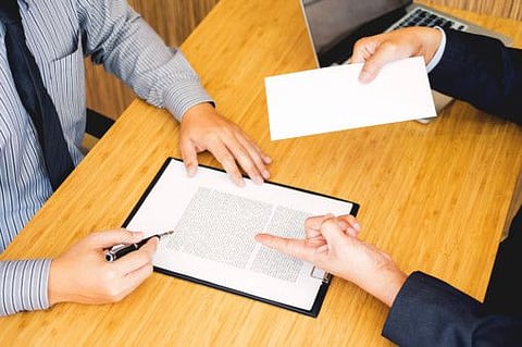 Hand of a businessman hands over a resignation letter final remuneration to executive boss on a wooden table to his boss Change of job, unemployment concept. (Hand of a businessman hands over a resignation letter final remuneration to executive boss o