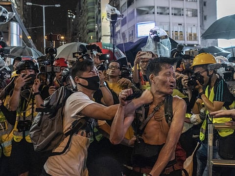A man is attacked by a masked man, both surrounded by journalists, in the Kowloon area of Hong Kong, Oct. 6, 2019. (Adam Dean/The New York Times)