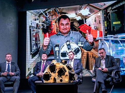 Russian cosmonaut Alexey Ovchinin (on screen) gestures in the International Space Station (ISS) as he poses with the 3D bioprinter developed in Russia during a press conference in Moscow on October 9, 2019.