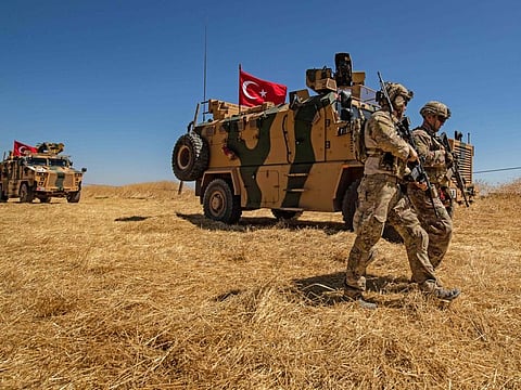 US troops walk past a Turkish military vehicle during a joint patrol in the Syrian village of Al Hashisha on the outskirts of Tal Abyad town along the border on September 8, 2019.