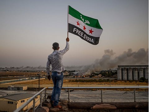 A man waves a Syrian opposition flag reading "Free Syria" on October 13, 2019 in Akcakale as smoke rises in the background from the Syrian border city of Tal Abyad seized today by Turkish forces and their proxies, on the fifth day of a Turkish offensive in Syria against Kurdish-controlled areas