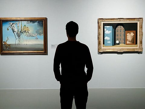 A museum assistant poses in front of paintings of surrealist artists Salvador Dali of Spain and Rene Magritte of Belgium