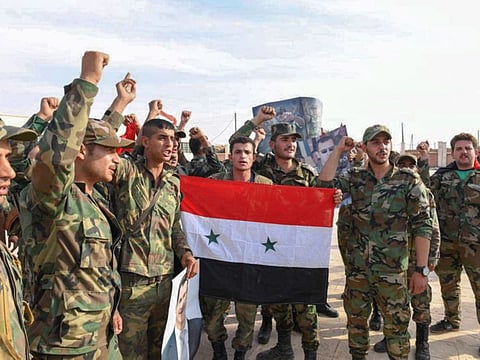 A handout picture released by the official Syrian Arab News Agency (SANA) on October 15, 2019 shows a Syrian army troops posing with a national flag after reportedly completing their deployment in the Syrian northern city of Manbij.