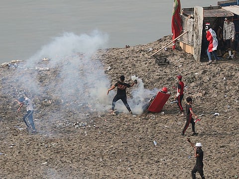 An anti-government protester prepares to throw back a tear gas canister fired by Iraq security forces to disperse a during a demonstration, in Baghdad, Iraq, Wednesday, Oct. 30, 2019.