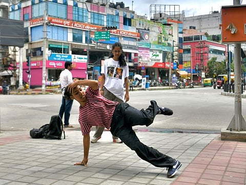 Breakdancer Johanna Rodrigues performs a dance move on a street while another performer looks on in Bangalore.