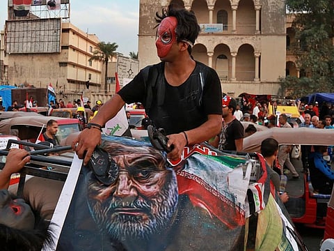 In this Nov. 3, 2019, file photo, protester hits a poster showing the leader of the Iranian Revolutionary Guard's foreign wing, or Quds Force, Gen. Qassim Soleimani with a shoe during ongoing anti-government protests in Baghdad, Iraq.