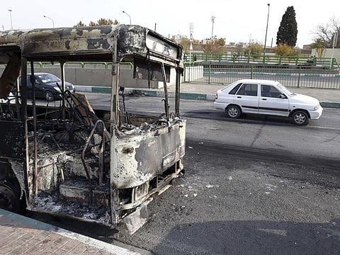 This photo released by the Iranian Students' News Agency, ISNA, shows cars drive past a scorched public bus that remained on the street after protests.