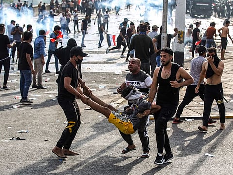 In this file photo taken on October 01, 2019, Iraqi protesters carry away an injured comrade amid clashes with riot police during a demonstration against state corruption and poor services, at Baghdad's Tahrir Square.