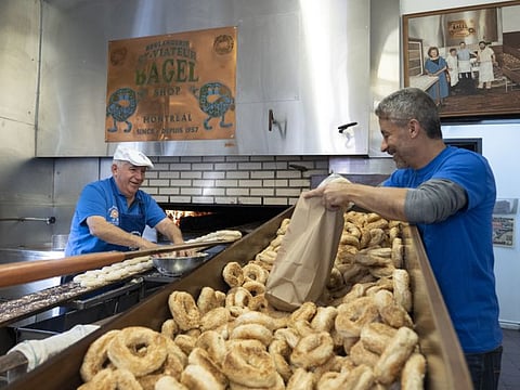 Joe Morena, left, the owner of St-Viateur Bagel, prepares a batch of bagels in a wood-burning oven in Montreal, Quebec, Canada on Nov. 8, 2019. A culinary symbol of Montreal has become ensnared in a battle pitting environmentalists who want to abolish the pollutant-producing ovens against bagel-loving traditionalists.