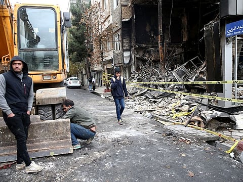 People walk near a burnt bank, after protests against increased fuel prices, in Tehran.