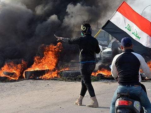A demonstrator holds an Iraqi flag near burning tires during ongoing anti-government protests in Nassiriya, Iraq November 24, 2019.