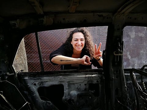 Lebanese protester Farah Merhi poses with her burnt-out car, flashing a peace sign.