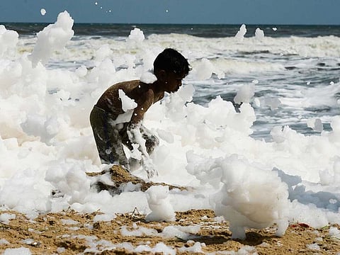 A youth plays over foamy discharge, caused by pollutants, as it mixes with the surf at a beach in Chennai