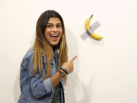 People post in front of Maurizio Cattelan's "Comedian" presented by Perrotin Gallery and on view at Art Basel Miami 2019 at Miami Beach Convention Center.