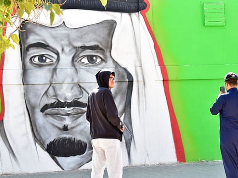 A Saudi man takes a photograph of a mural painting showing King Salman bin Abdulaziz on Tahliya street as another looks on, in the capital Riyadh on December 5, 2019.