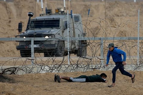 Palestinian demonstrators take cover in front of Israeli troops during a protest at the Israel-Gaza border fence