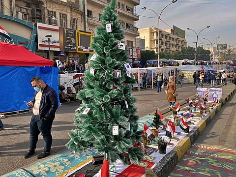 People pass by a Christmas tree with portraits of anti-government protesters who killed under fire from security forces in Tahrir Square during ongoing protests in Baghdad, Iraq, Thursday, Dec. 12, 2019. A gunman shot dead several people, including four protesters, Thursday provoking some anti-government demonstrators to disarm and hang him in a central Baghdad square, security and health officials said. The incident was condemned by the wider protest movement based in Tahrir Square, the epicenter of the movement, who said the individuals who killed the gunman were not part of their peaceful demonstrations.