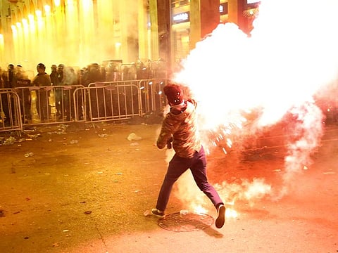 An anti-government protester throws flares against the riot police, background, during a protest near the parliament square, in downtown Beirut, Lebanon, Sunday, Dec. 15, 2019.