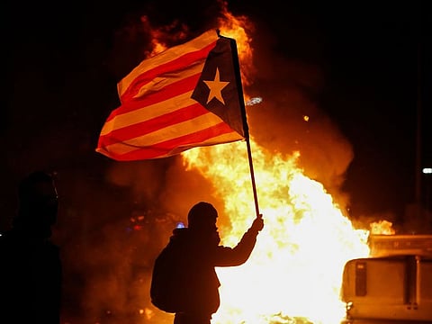 A protester waving a Catalan pro-independence "Estelada" flag stands next to a burning barricade during a protest called by Catalan separatist movement Democratic Tsunami outside the Camp Nou stadium in Barcelona on December 18, 2019.