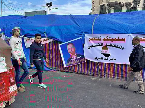 Anti-government protesters walk past a poster with a defaced picture of the governor of the southern Basra province Asaad al-Eidani and Arabic that reads "rejected by the people," during the ongoing protests, in Tahrir square, in Baghdad, Iraq, Wednesday, Dec. 25, 2019.