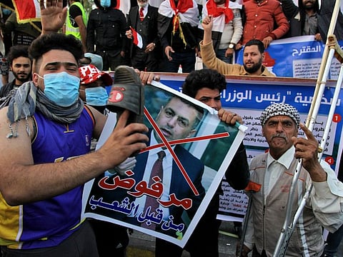 A protester hits a poster with a defaced picture of Asaad al-Eidani, Iran-backed parliamentary bloc's nominee for the post of the prime minister and Arabic that reads "rejected by the people," with a shoe during anti-government demonstrations in Baghdad, Iraq, Thursday, Dec. 26, 2019.